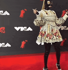 a woman wearing a mask is standing on a red carpet in front of a wall with vma logos