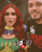 a woman with red hair is standing next to a man wearing a rb d shirt