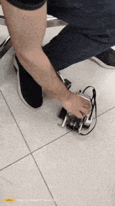 a person is kneeling down next to a small robot on the floor .