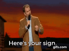 a man in a suit is holding a microphone and saying `` here 's your sign '' .