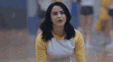 a woman wearing a yellow and white shirt is sitting on the floor .