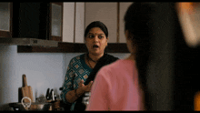 a woman in a pink shirt is talking to a woman in a kitchen