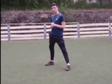 a young man in a blue shirt and black pants is standing on a field .