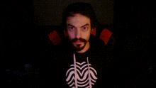 a man with a beard is wearing a black sweatshirt with a spider on it