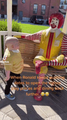 a baby stands next to a mcdonald 's statue