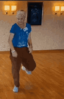 a woman in a blue shirt is dancing on a hardwood floor