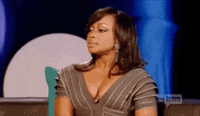 a woman in a gray dress is sitting on a couch with a blue background .