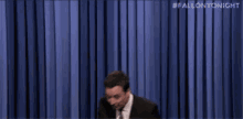 a man in a suit and tie is dancing in front of a blue curtain with the hashtag #fallontonight