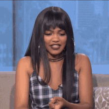 a woman with long hair is sitting on a couch wearing a plaid tank top