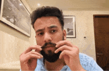 a man with a beard is adjusting his mustache while looking at the camera .