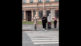 a group of people are walking across a crosswalk with a stroller