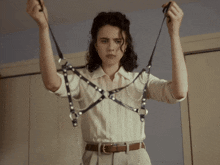 a woman in a white shirt is holding a harness with pearls on it