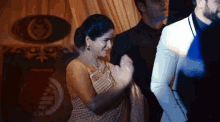a woman in a sari is applauding a man in a white suit .