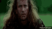 a man with blood on his face is standing in a field looking at the camera .