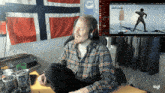 a man in a plaid shirt sits in front of a computer screen that says logi on the bottom