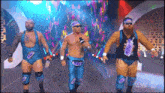 three men in blue wrestling outfits are walking on a stage with a microphone .