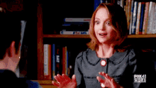 a woman talking to a man in front of a bookshelf .
