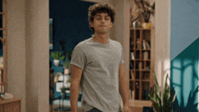 a young man in a grey t-shirt is standing in a living room