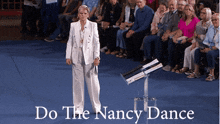 a woman in a white suit stands in front of a crowd with the words do the nancy dance written below her