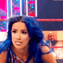 a woman with blue hair is standing in a wrestling ring looking at the camera .