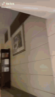 a tiktok video of a woman walking down a hallway with a picture on the wall