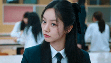 a young woman in a school uniform and tie is looking at the camera .