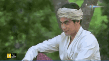 a man wearing a turban and a white shirt is sitting on a purple pillow .