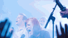 a woman singing into a microphone with a man behind her