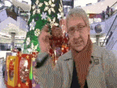 a man with glasses stands in front of a christmas tree