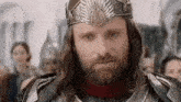 a man with a beard and a crown on his head is wearing armor and a crown .
