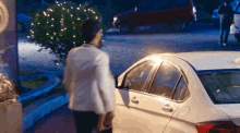 a man in a white suit is walking towards a white car at night
