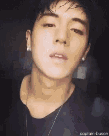 a close up of a young man wearing a black shirt and a necklace .