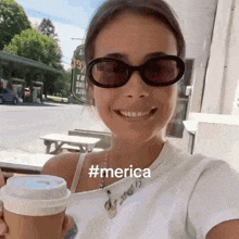 a woman wearing sunglasses is smiling while holding a cup of coffee .