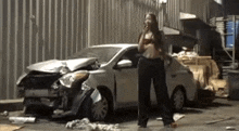 a woman is standing in front of a damaged car and talking on a cell phone .