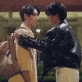 a man in a black leather jacket is hugging another man
