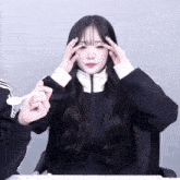 a girl in a black jacket holds her hands to her forehead