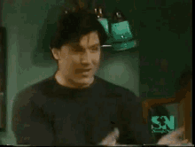 a man and a woman are standing next to each other in a room with a green sn logo in the corner