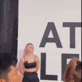 a woman in a black crop top is standing in front of a sign that says at