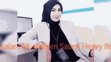a woman wearing a hijab and a lanyard with the letter b on it sits at a desk