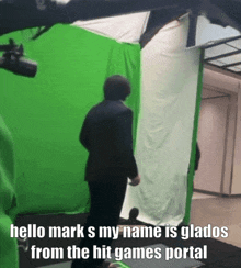 a man in a suit is standing in front of a green screen with the words hello mark s my name is glados from the hit games portal