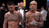 two men are standing next to each other in a boxing ring and one of them has a tattoo on his chest ..