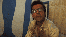 a man wearing glasses is sitting in front of a blue and white striped wall