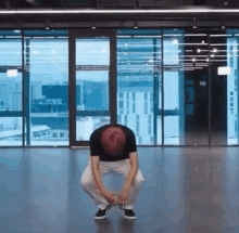 a man is squatting on the floor in front of a large window in a room .