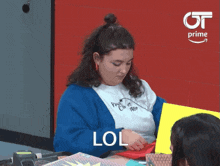 a woman in a blue cardigan is sitting at a table with lol written on her face