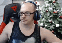 a bald man wearing glasses and headphones sitting in front of a christmas tree .