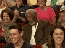 a man in a suit and tie is sitting in a crowd of people laughing .