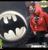 a woman in a red jacket is standing in front of a batman logo