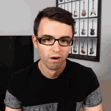 a man wearing glasses is standing in front of a guitar wall