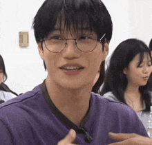 a young man wearing glasses and a purple shirt looks at the camera