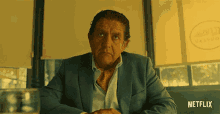 a man in a suit and tie is sitting at a table with a netflix logo in the corner